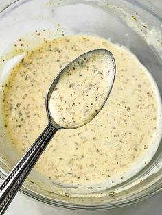 a spoon in a glass bowl filled with cream and seasoning next to two forks