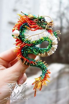 a hand holding a beaded dragon brooch