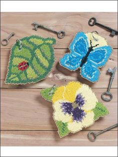 three cross stitch coasters on a wooden table with scissors and other crafting supplies