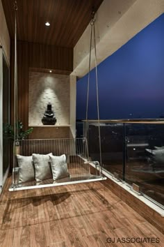 a balcony with wooden flooring and white pillows on the swing chair, overlooking city lights at night