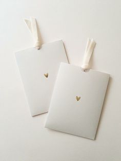 two white tags with gold hearts are on a white surface, one has a bow and the other has a heart