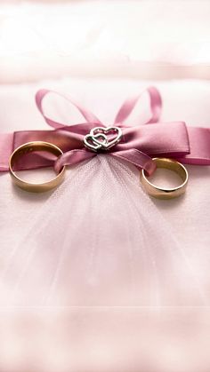 two gold wedding rings tied to a pink satin ribbon with a heart on the top