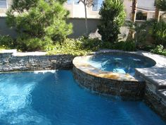 an outdoor swimming pool surrounded by stone walls and landscaping area with palm trees in the background