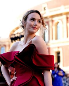 a woman in a red dress posing for a photo on the street with people behind her