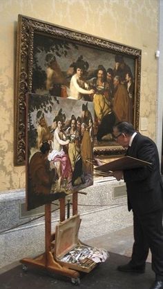 a man standing in front of a painting holding a piece of paper and looking at it