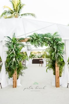 an outdoor wedding setup with white drapes and greenery on the side, surrounded by palm trees