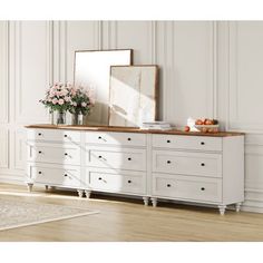 a white dresser with flowers and a mirror on the top, in front of a wall