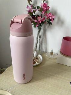 a pink cup sitting on top of a table next to a vase filled with flowers