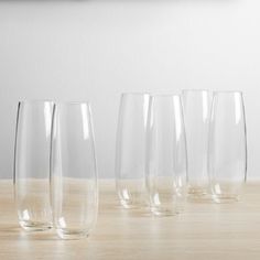 five clear wine glasses lined up on a wooden table in front of a white wall