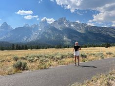 a woman standing on the side of a road in front of mountains