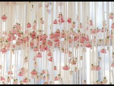 pink flowers hanging from the side of a window with sheer curtains in front of them