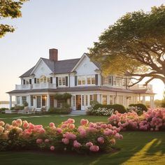 a large white house with lots of flowers in the front yard and trees around it