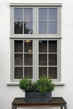 a bench sitting in front of a window with two potted plants next to it