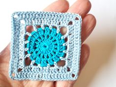 a hand holding a crocheted square with a blue center