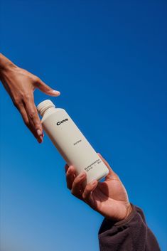 two hands reaching out to touch a white water bottle in front of a blue sky