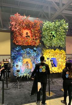 two people are standing in front of an art display with flowers on the wall behind them