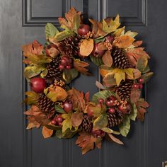 a wreath with apples, leaves and pine cones is hanging on the front door for fall