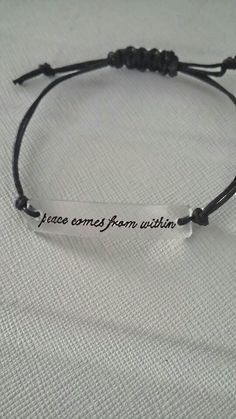 a bracelet that says peace comes from within on it with a black cord and an engraved message