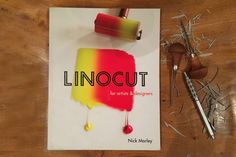 a book about linocut is sitting on a table next to scissors and thread