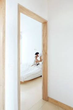 a woman sitting on top of a bed next to a mirror in a room with white walls