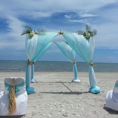 an outdoor wedding setup on the beach with blue draping and white linens