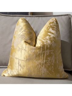 a gold pillow sitting on top of a gray couch next to a white and grey pillow