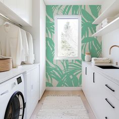 a washer and dryer in a small room with green palm leaves on the wall