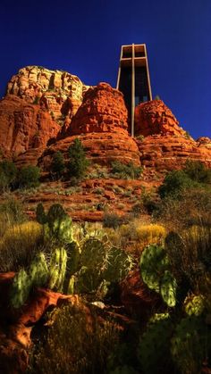 a tall tower sitting on top of a red rock covered hillside next to green plants