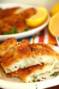 two white plates topped with food next to lemon wedges and breaded chicken patties