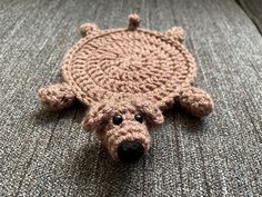 a crocheted teddy bear laying on top of a gray couch next to it's head