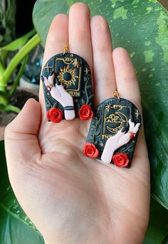 pair of earrings with red roses on black and gold plated earwires in hand