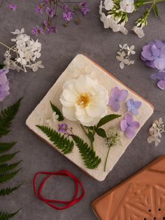 a white flower sitting on top of a plate next to purple flowers and greenery