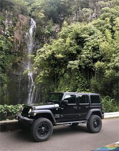 a black jeep parked in front of a waterfall on the side of a mountain road