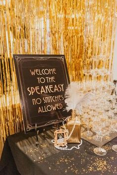 a welcome sign on a black table with gold streamers behind it and champagne glasses