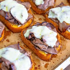 small sandwiches with meat and cheese on them sitting on a baking sheet, ready to be eaten