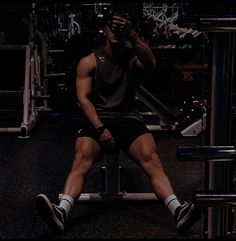 a man sitting on top of a gym bench taking a selfie with his cell phone