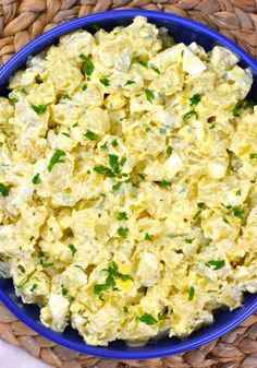 a blue bowl filled with potato salad sitting on top of a woven table cloth next to a basket