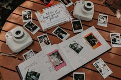 an open book with pictures and a camera on it sitting on a wooden table surrounded by photos