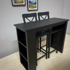 a black table with two chairs next to it and pictures on the wall behind it