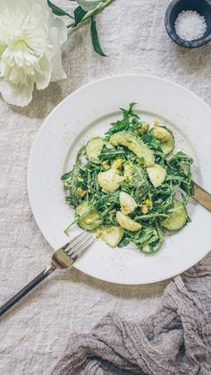 a white plate topped with green vegetables next to a fork and bowl filled with sauce