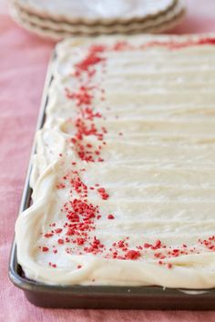 a cake with white frosting and red sprinkles sitting on a table