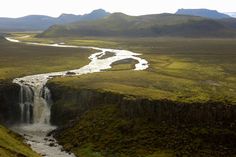 a river running through a lush green valley next to a tall mountain covered in grass