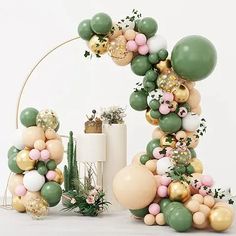 an arch made out of balloons and greenery on the floor next to a potted plant