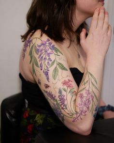 a woman with tattoos on her arms and chest sitting in front of a window holding her hands together