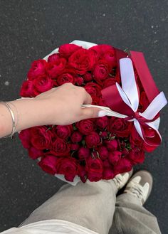 a person holding a bouquet of red roses in their hand with a white ribbon around it