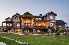 a large house with lots of windows and lights on it's front porch, surrounded by green grass