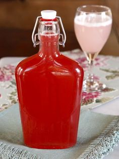 a red bottle sitting on top of a table next to a glass filled with liquid