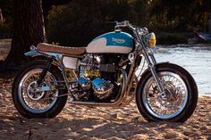 a blue and white motorcycle parked on top of a sandy beach next to a tree