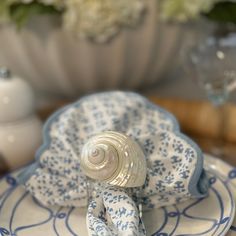 a blue and white plate with a shell on it's centerpiece, next to a vase filled with flowers