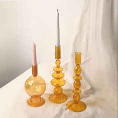 three yellow glass candlesticks sitting next to each other on a white cloth covered table